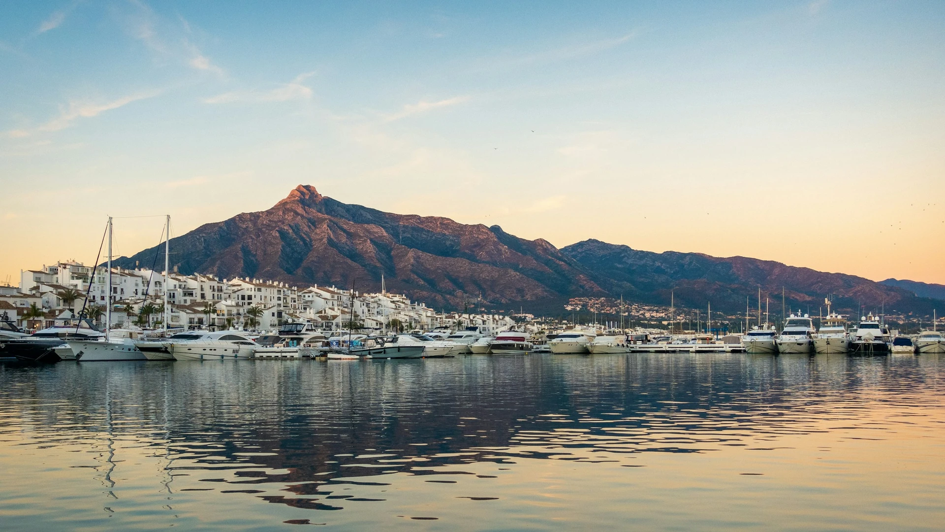Barcos en un puerto de Marbella con edificios blancos y montañas al fondo