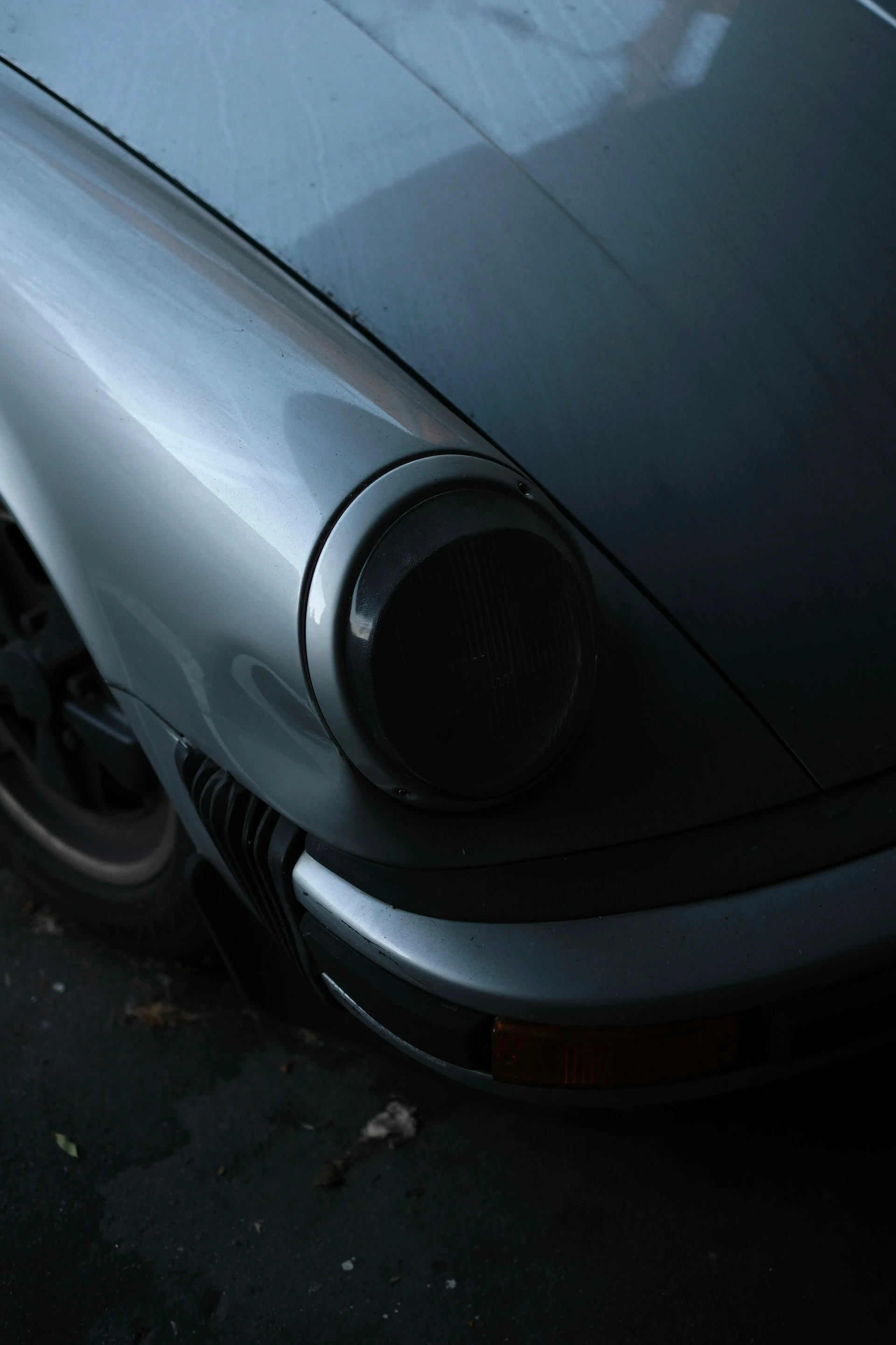 Faro redondo y carrocería plateada de un Porsche clásico entre sombras
